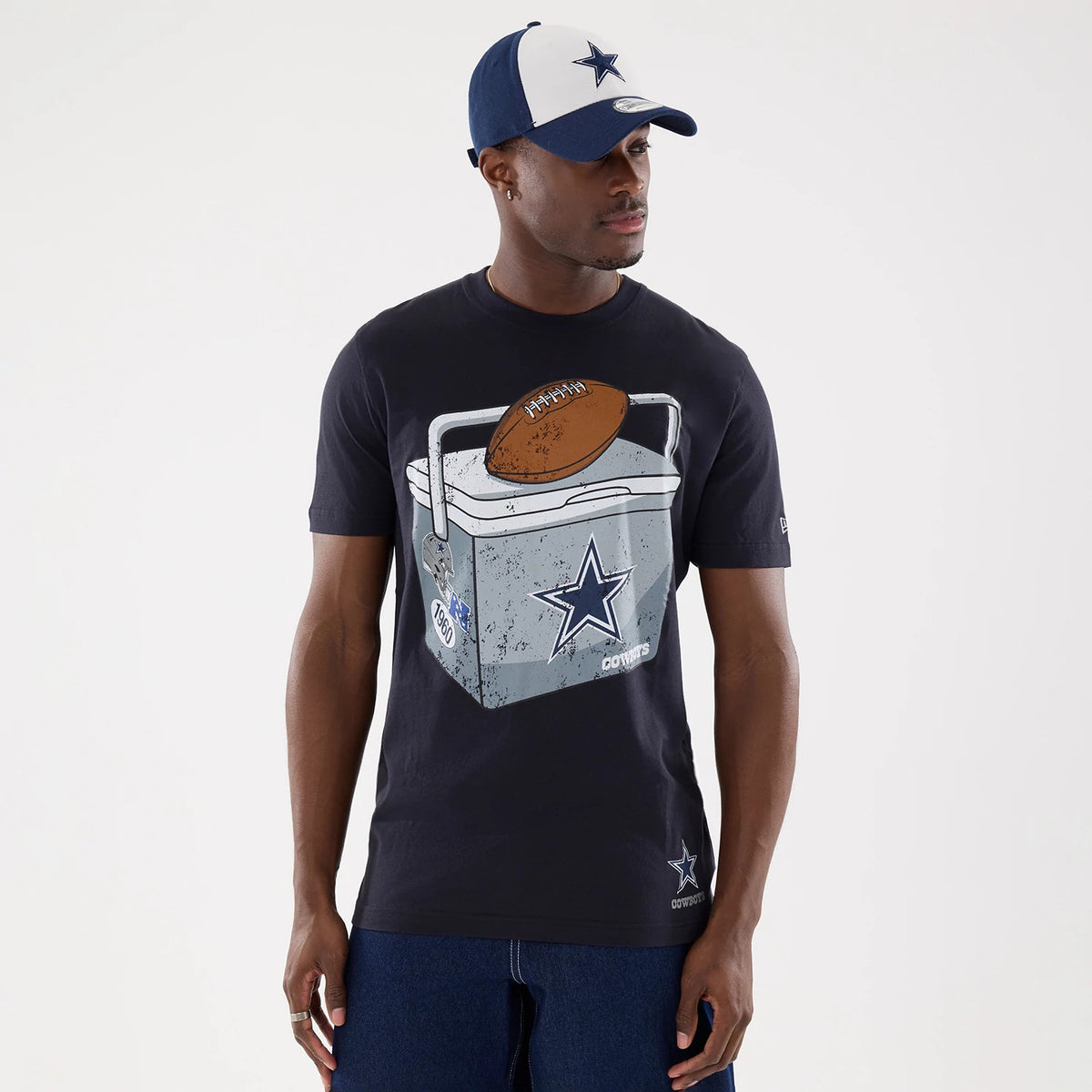 New Era Dallas Cowboys NFL Training 2026 Navy T-Shirt, front view on-model showing a large graphic of a cooler with a football on it, the Cowboys star logo prominently displayed, and a smaller embroidered Cowboys star logo at the bottom front.