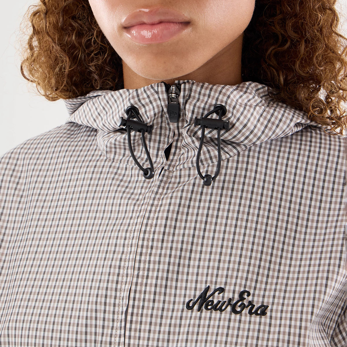 Womens New Era Check Beige Oversized Windbreaker Jacket, front view showing a drawstring hood with black toggles, a zip closure, a beige check pattern, and an embroidered New Era logo on the left chest.