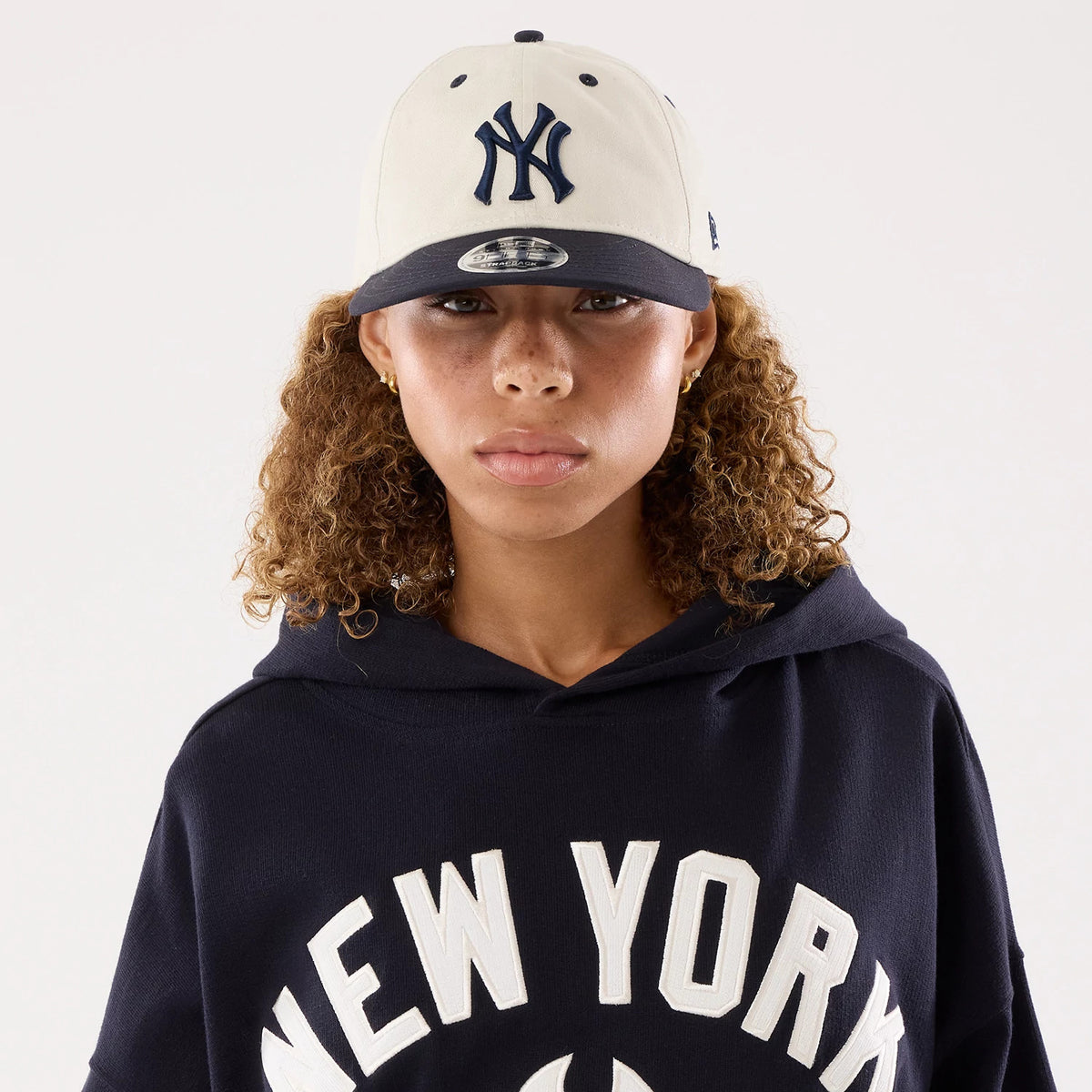 New Era New York Yankees Womens MLB Navy Oversized Pullover Hoodie, front view on a model wearing a matching cap, showing New York lettering across the chest in white, with a spacious hood draped over the shoulders.