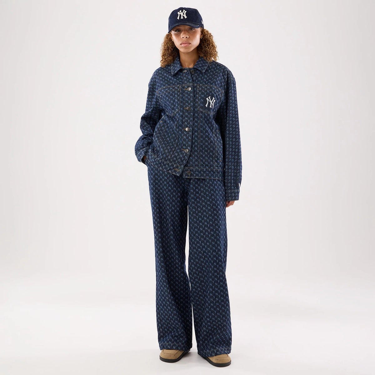 New Era New York Yankees Womens MLB Denim Navy Wide Leg Trousers, front view on a model with a matching denim jacket, showing a navy all-over Yankees logo pattern, wide legs, and a relaxed fit styled with neutral-toned footwear.
