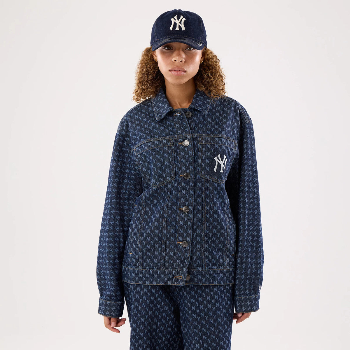 New Era New York Yankees Womens MLB Denim Navy Jacket, front view on a model, showing a button-up design with an all-over NY pattern, embroidered white Yankees logo on the left chest, and styled with a matching navy cap featuring the same logo.