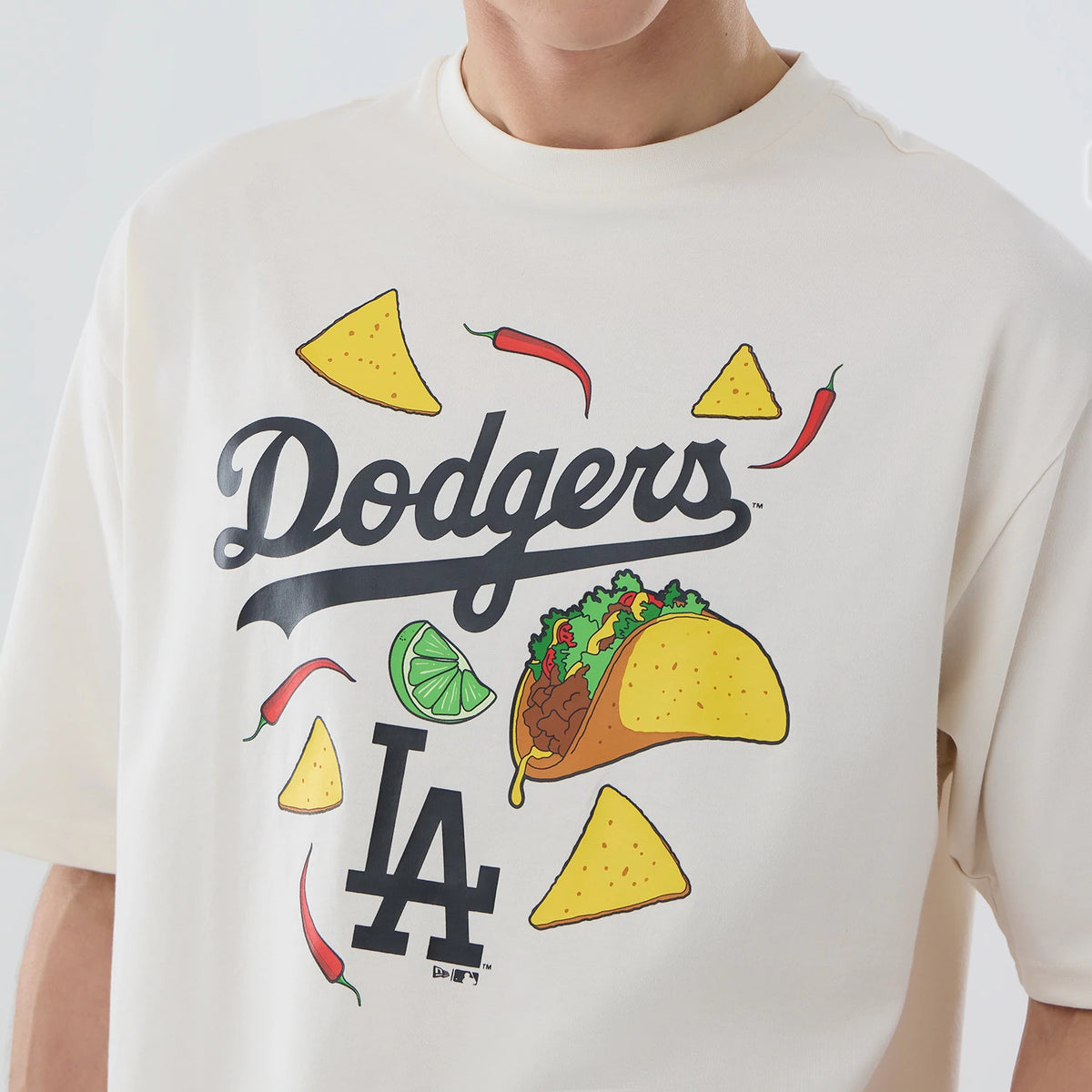New Era LA Dodgers MLB Food Graphic Open White Oversized T-Shirt, front view featuring a printed Dodgers logo at the centre, surrounded by food illustrations including a taco, lime wedge, red chillies, tortilla chips and the LA logo beneath.