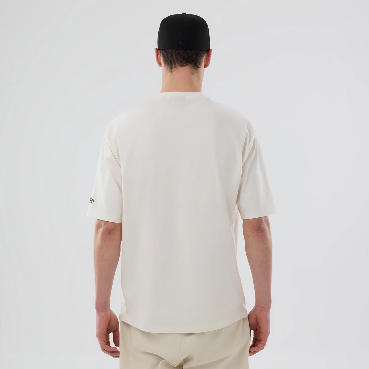 New Era LA Dodgers MLB Food Graphic Open White Oversized T-Shirt, back view on a model featuring a plain white back with short sleeves, a small embroidered New Era logo on the left sleeve, and paired with neutral trousers and a black cap.