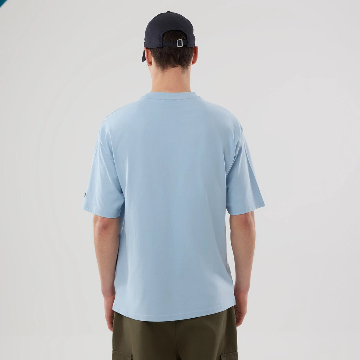 New Era New York Yankees MLB Food Graphic Pastel Blue Oversized T-Shirt, back view on a model wearing a dark cap, showcasing the pastel blue colour of the oversized t-shirt, with short sleeves and a small embroidered New Era logo on the left sleeve.