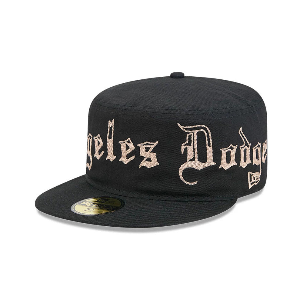 LA Dodgers MLB Heritage Black New Era Pillbox Cap, three-quarter view showing raised beige embroidered Los Angeles Dodgers lettering across the front, a flat black visor with a gold size sticker, and the New Era flag logo on the left side.