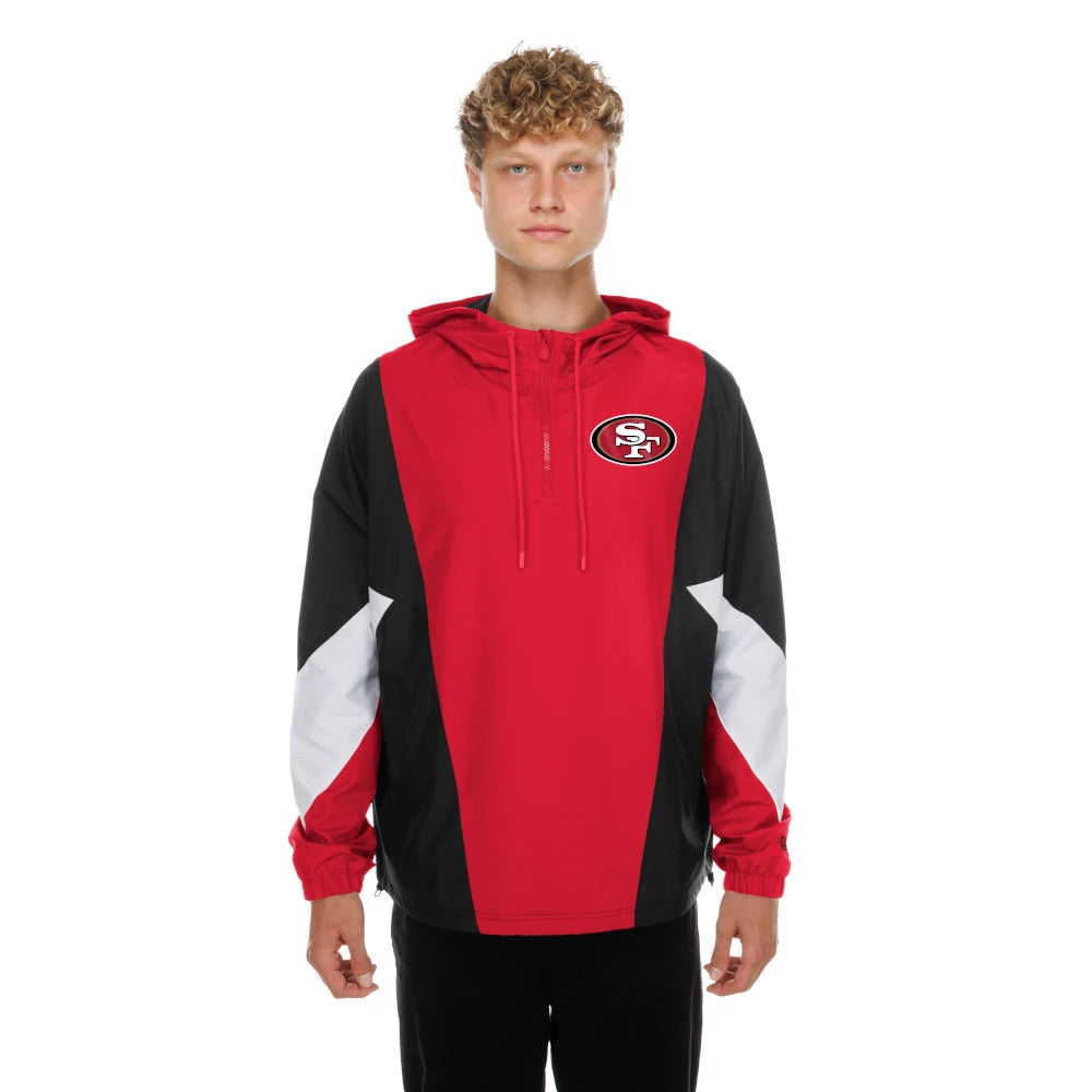 New Era San Francisco 49ers NFL Red Windbreaker Jacket, front view on a model showing the red body with black and white panels, an embroidered SF logo on the chest, and a drawstring hood creating a sporty, team-focused look.