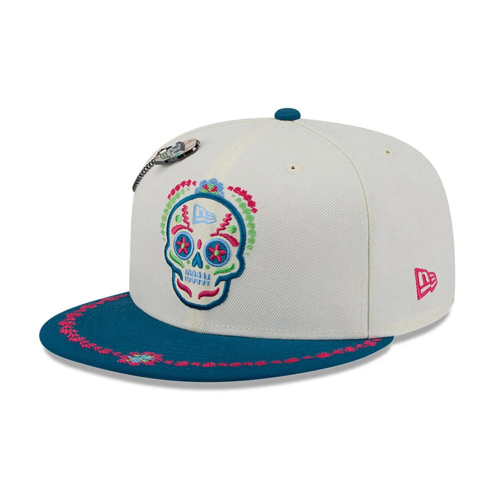 New Era Day Of The Dead Light Beige & Blue 59FIFTY Fitted Cap, three-quarter view with an intricately embroidered multi-coloured sugar skull design on the front panel, a blue flat visor with pink floral accents.
