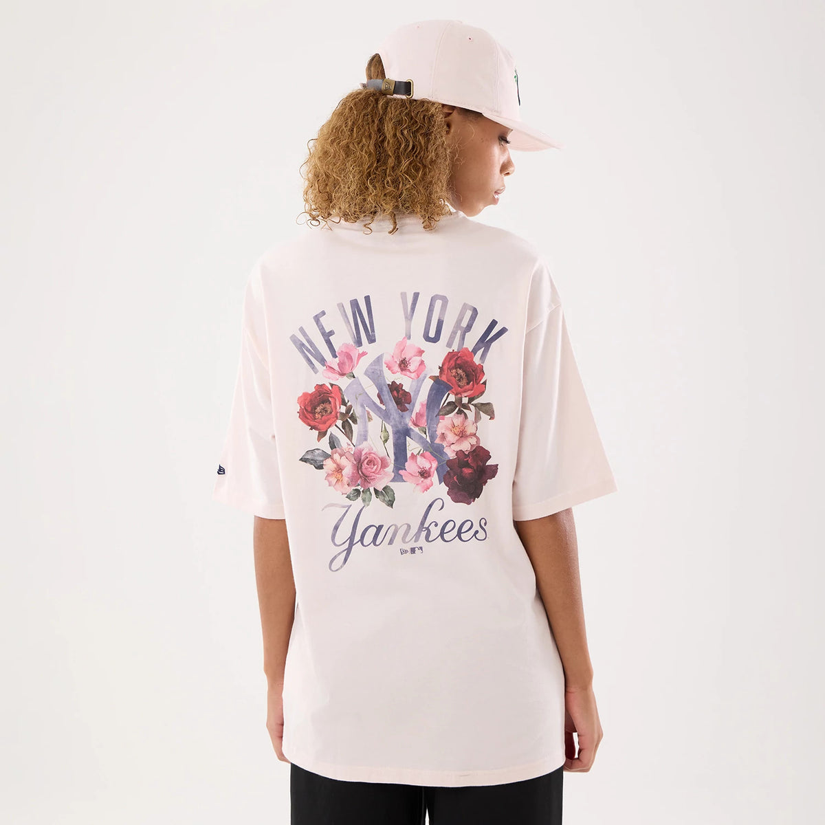 New Era New York Yankees Womens MLB Graphic Pastel Pink T-Shirt, back view on-model displaying large New York lettering and floral graphics surrounding the NY logo, with Yankees written below and a New Era embroidered logo on the sleeve.