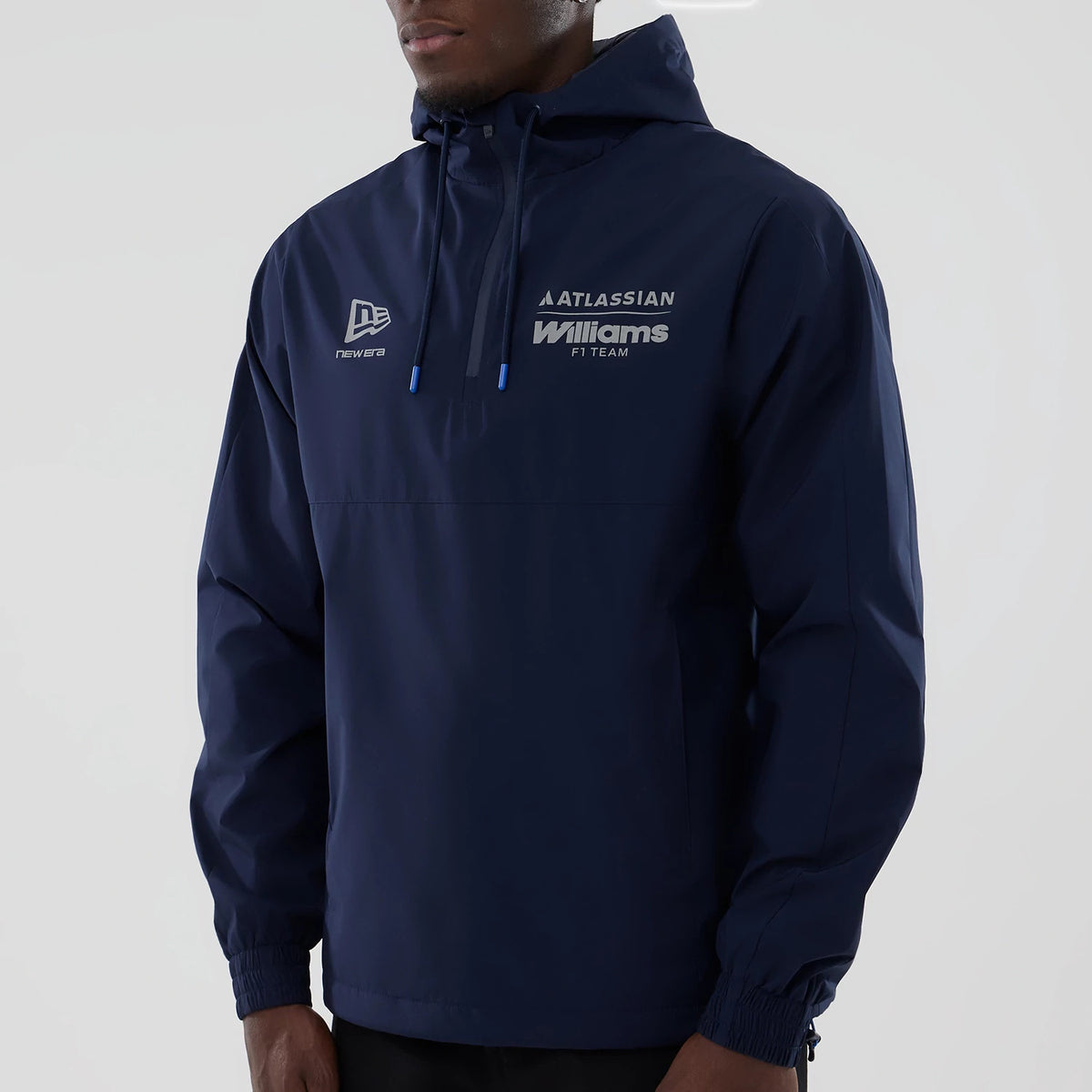 New Era Williams Navy Windbreaker Jacket, front view on a model featuring a navy-blue design with a raised New Era logo on the left chest, Williams F1 Team text on the right, and a drawstring hood with blue accents and elasticated cuffs.