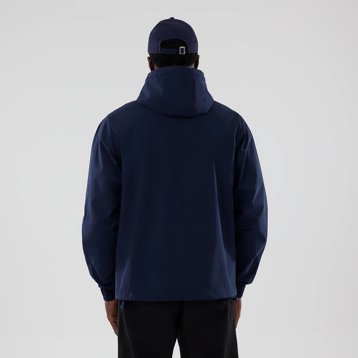 New Era Williams Navy Windbreaker Jacket, back view on a model wearing a matching cap, highlighting the high collar and hood, navy fabric with an uninterrupted design, and elasticated cuffs at the wrists providing a simple and appearance.