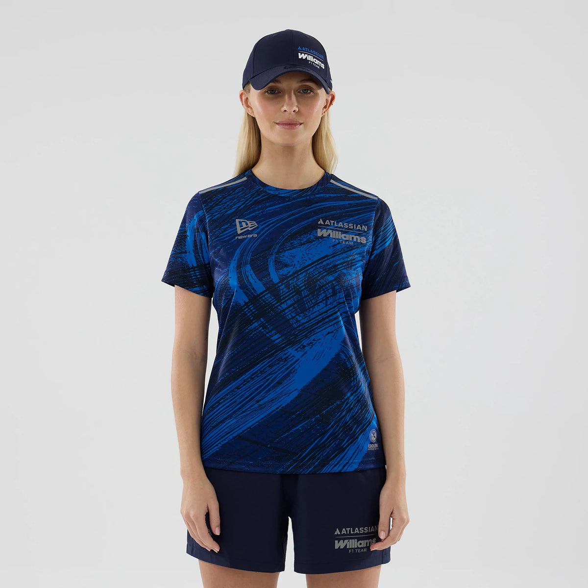 New Era Williams Womens Navy Active T-Shirt, front view on a model with matching navy shorts and cap, featuring a dynamic blue graphic pattern across the body, with an embroidered New Era logo on the chest and Williams branding on the upper left.