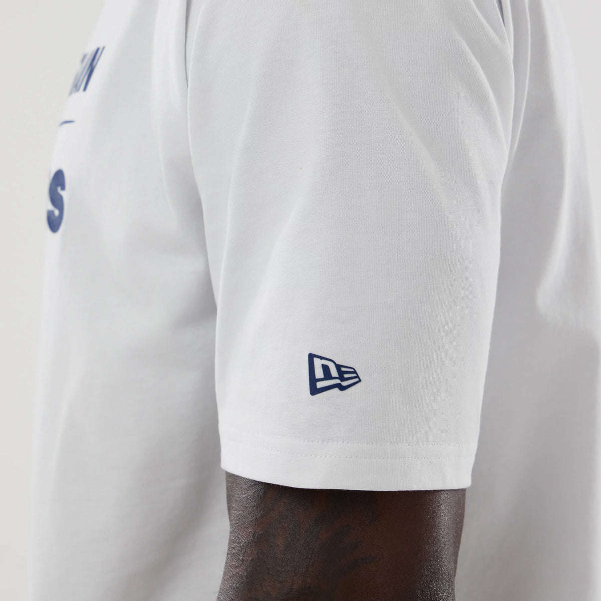 New Era Williams White Oversized T-Shirt, side view showcasing the clean white fabric with a blue embroidered New Era logo on the left sleeve, view of the shoulder seam, and arm with continuous white tone surrounding the design.