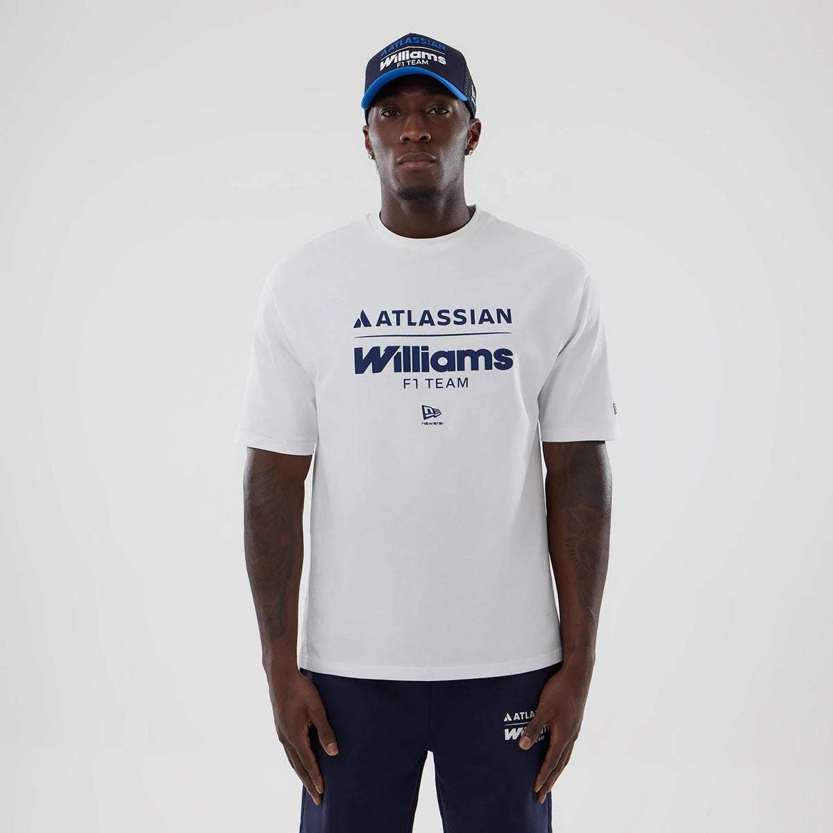 New Era Williams White Oversized T-Shirt, front view on a model styled with a matching cap, featuring navy blue Atlassian and Williams F1 Team lettering across the chest, and a small embroidered New Era logo below the text.