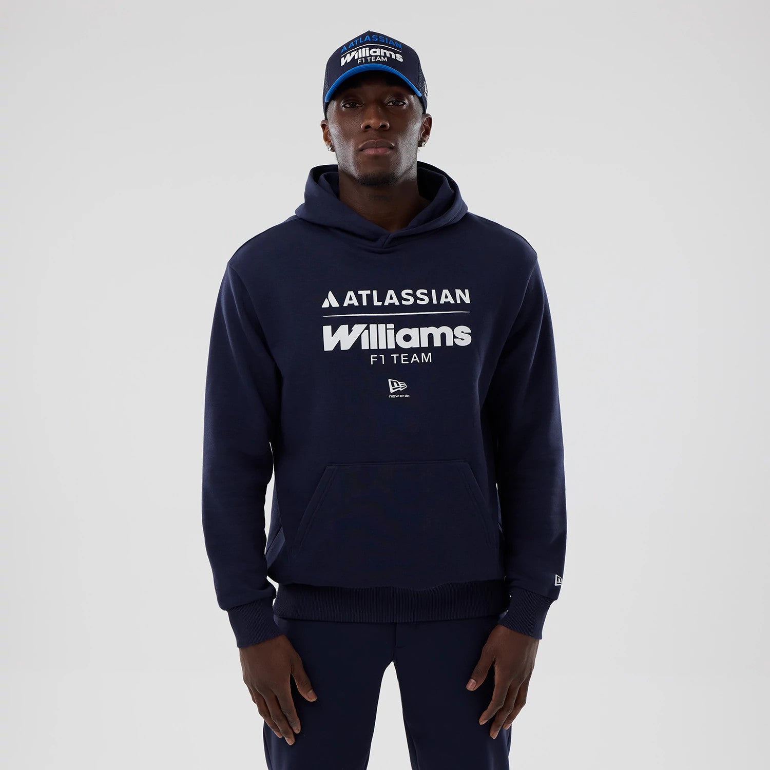 New Era Williams Navy Oversized Pullover Hoodie, front view on-model featuring large white printed Atlassian and Williams F1 Team logos across the chest, a kangaroo pocket at the lower front, and a small embroidered New Era logo on the sleeve cuff.