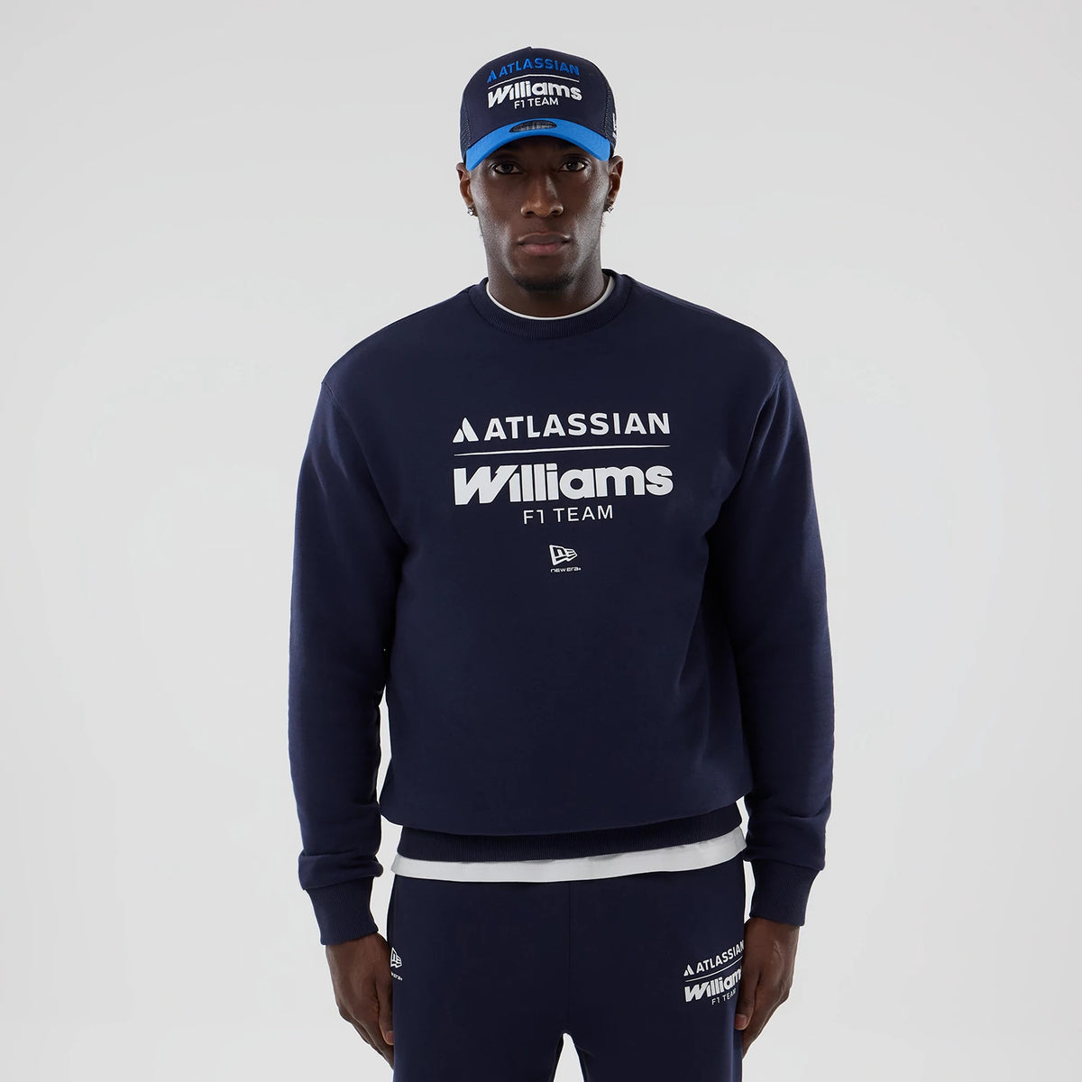 New Era Williams Navy Oversized Crewneck Sweater, front view on a model with matching navy trousers, featuring white Atlassian and Williams F1 Team logos across the chest, alongside a small embroidered New Era logo above the left hip.