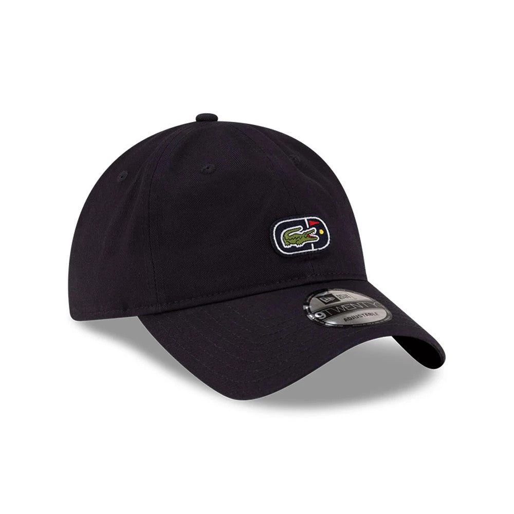 Lacoste X New Era Navy 9TWENTY Adjustable Cap, three-quarter view showing the embroidered Lacoste crocodile logo on the front panel, the curved navy visor with a 9TWENTY size sticker, and the round top button with eyelets on the crown.