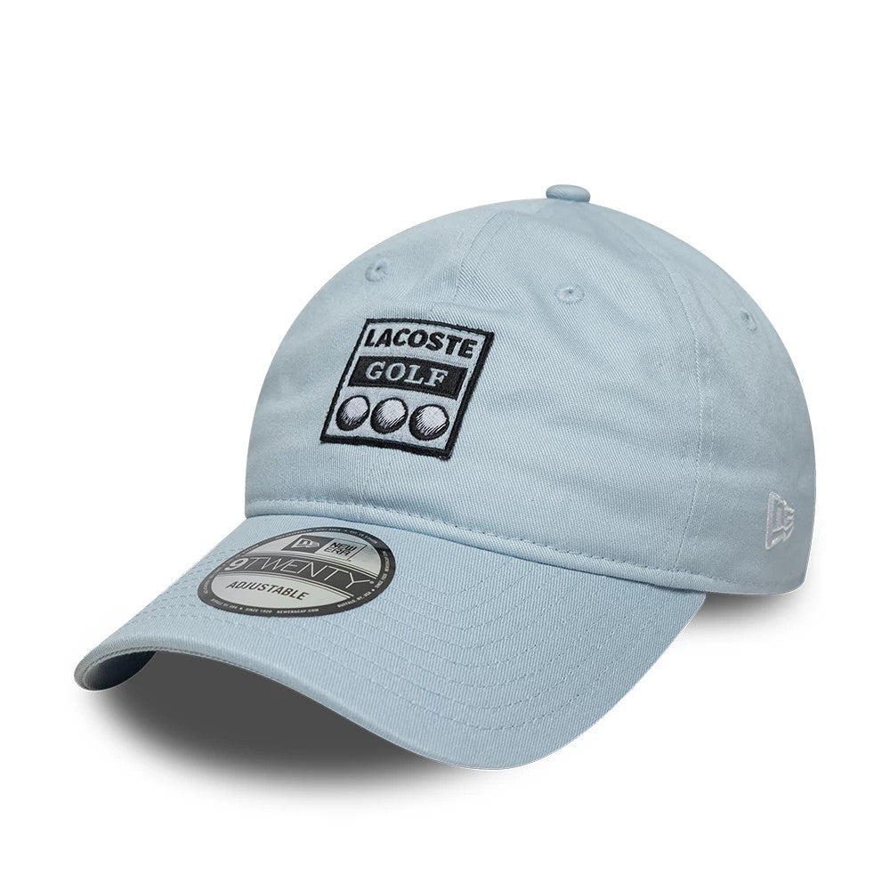 Lacoste X New Era Pastel Blue 9TWENTY Adjustable Cap, front view showing a black and white embroidered Lacoste Golf logo on the unstructured pastel blue crown, curved visor with 9TWENTY size sticker, and New Era flag on the left side.