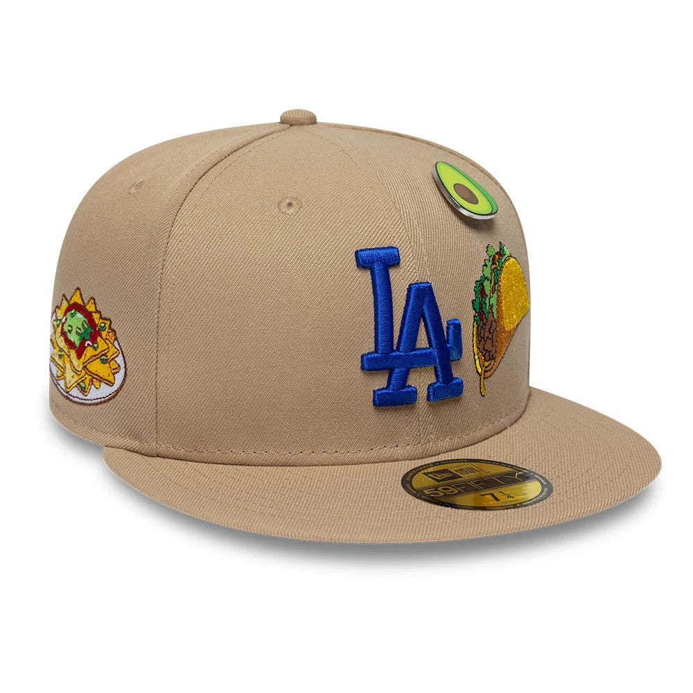 LA Dodgers MLB Food Beige New Era 59FIFTY Fitted Cap, three-quarter view showing a blue embroidered LA logo on the front panel, colourful taco and avocado graphics on the crown, and a gold 59FIFTY size sticker on the flat beige visor.