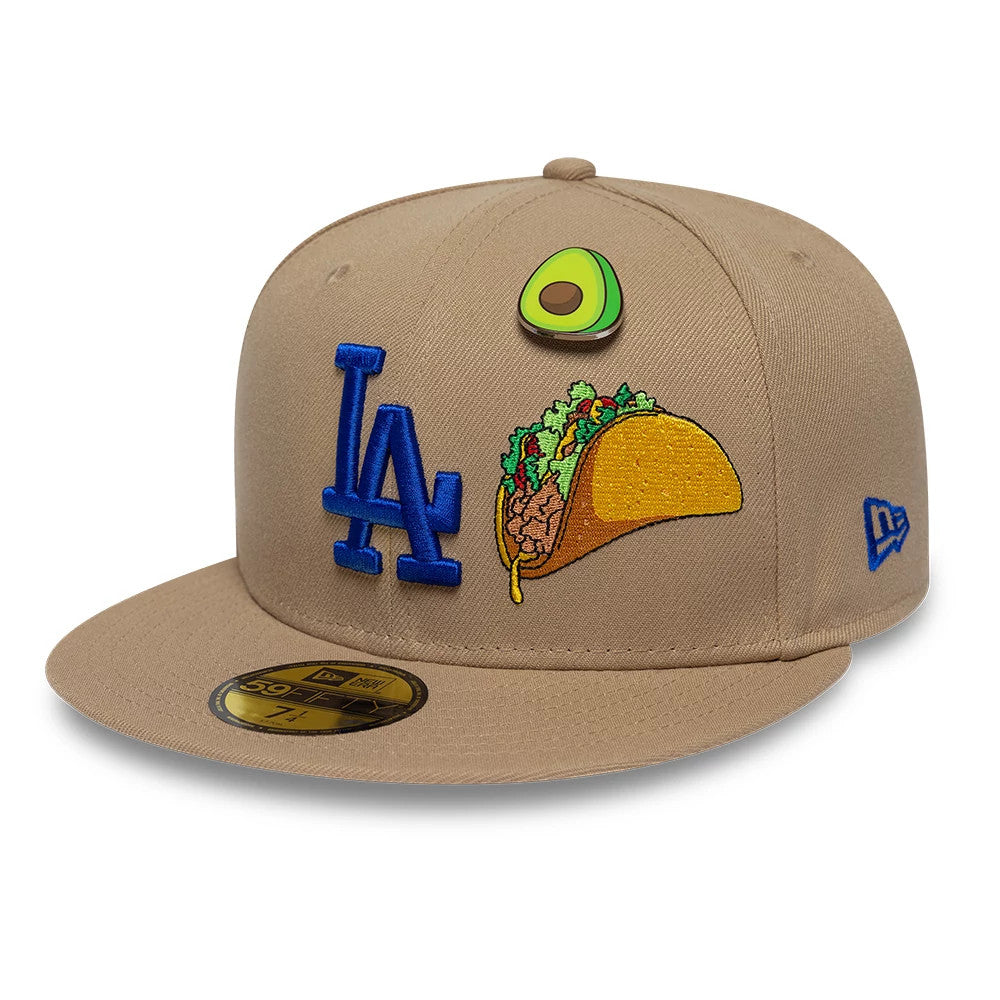 LA Dodgers MLB Food Beige New Era 59FIFTY Fitted Cap, three-quarter view showing a blue embroidered LA logo and taco graphic on the front panel, a gold 59FIFTY size sticker on the beige flat visor, and an avocado pin on the crown.