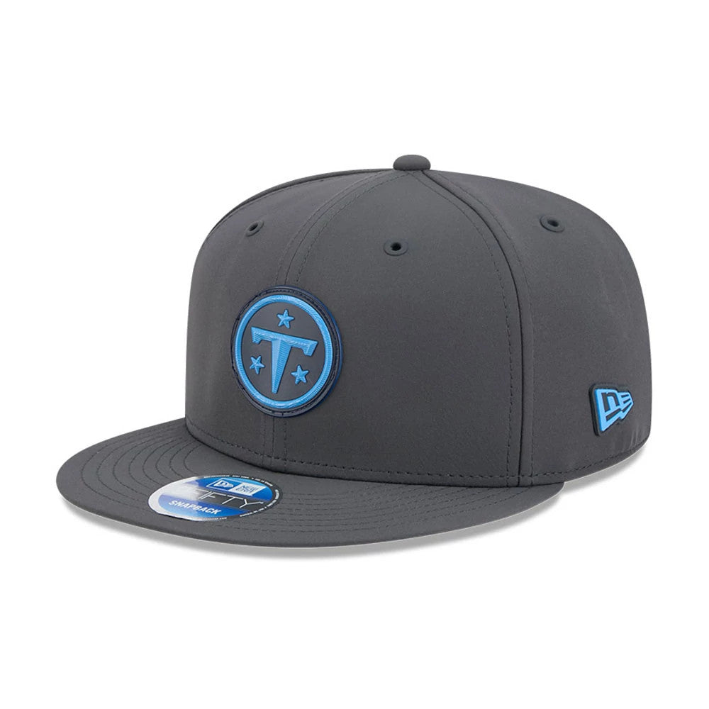 Titans NFL Sideline 2026 Charcoal New Era 9FIFTY Snapback Adjustable Cap, three-quarter view showing the blue embroidered Titans logo on the front panel, a matching blue New Era flag logo on the left side, and a 9FIFTY size sticker on the visor.