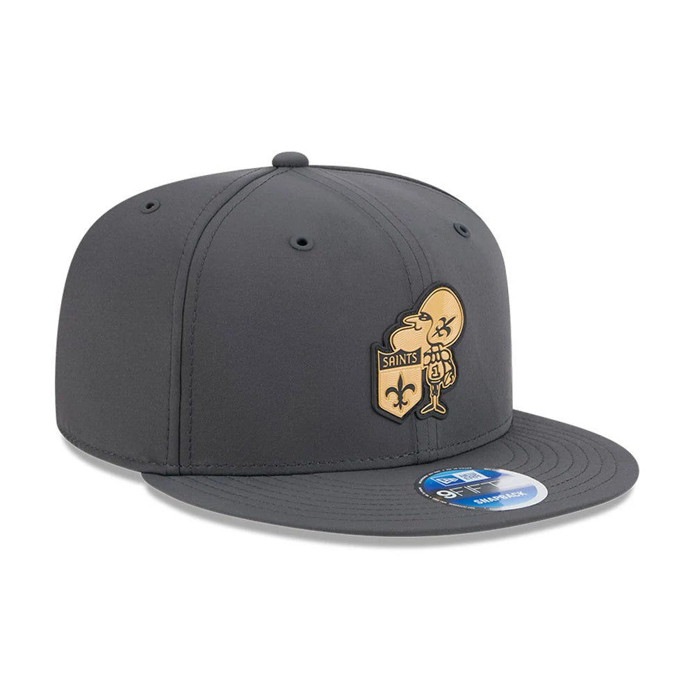 Saints NFL Sideline 2026 Charcoal New Era 9FIFTY Snapback Adjustable Cap, front view showing a gold and black Saints logo on the front panel, a charcoal flat visor, and a blue and white 9FIFTY size sticker on the visor.