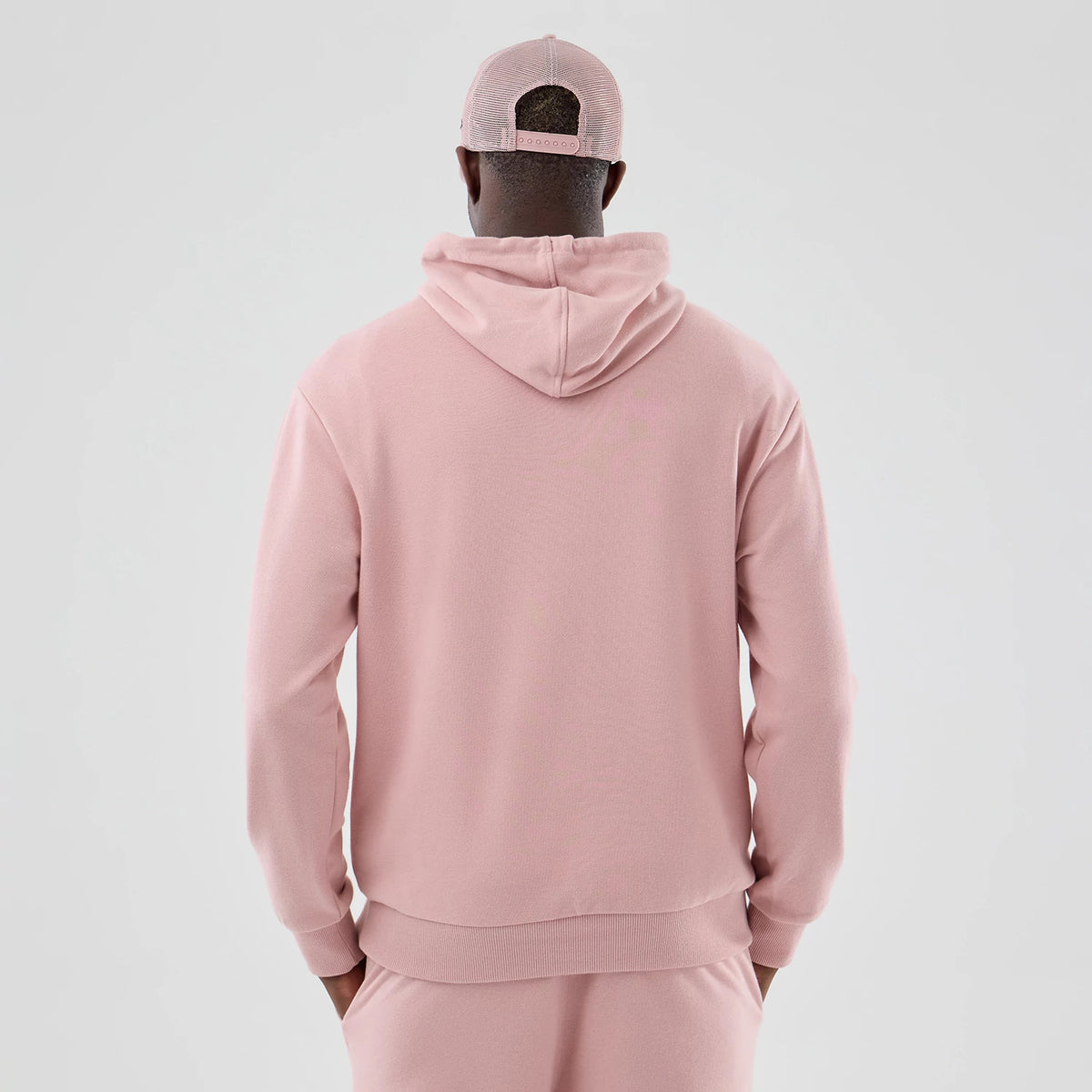 New Era Dodgers MLB Midi League Essential Pastel Pink Oversized Pullover Hoodie, back view on a model highlighting the relaxed fit and attached hood with its drape, paired with matching pastel pink trousers and a cap with an opening.