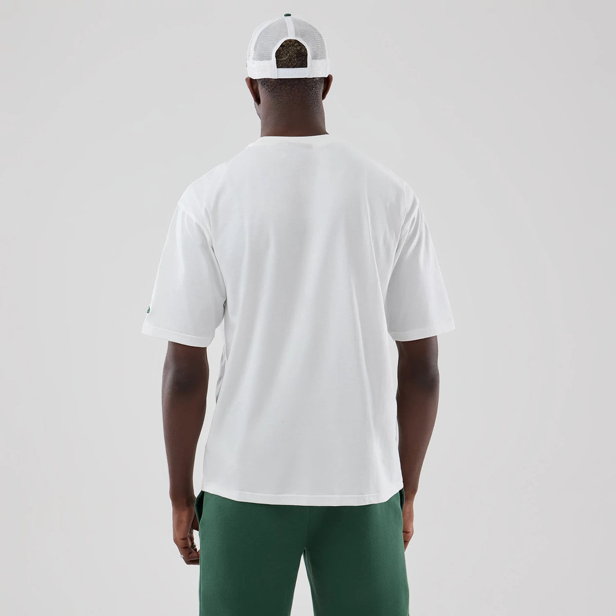 New Era New York Yankees MLB Midi League Essential White Oversized T-Shirt, back view on-model showing the plain white back with short sleeves, paired with green trousers and a white mesh back cap, completing the casual look from behind.