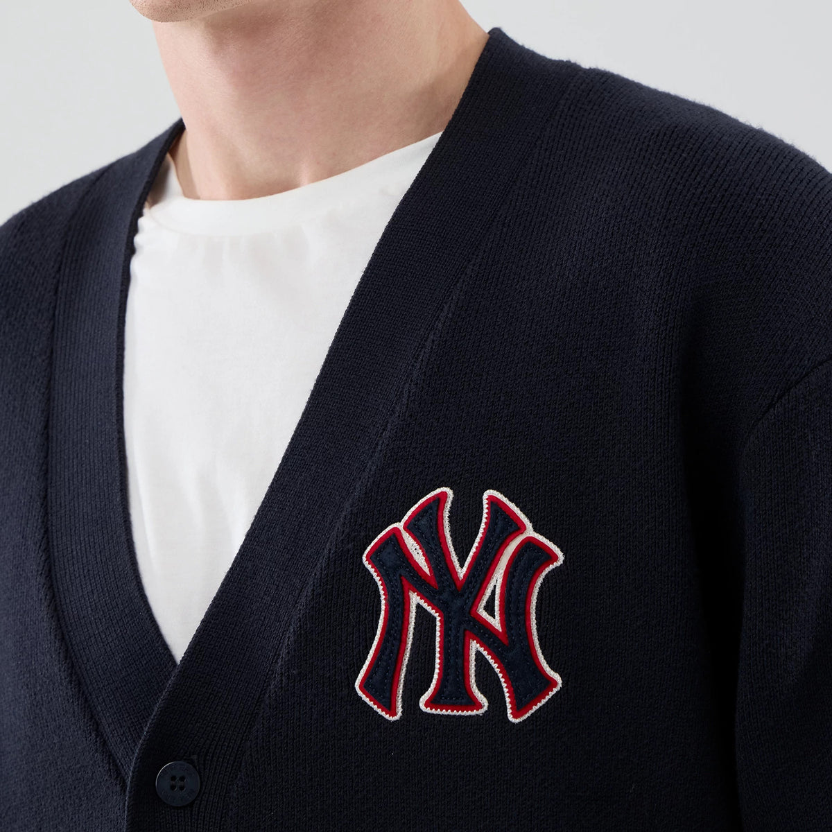 New Era New York Yankees MLB Knit Navy Cardigan, front view on a model showing the large ‘NY’ logo in red and white embroidery on the left chest, a black button fastening, and a ribbed V-neck collar over a white T-shirt.