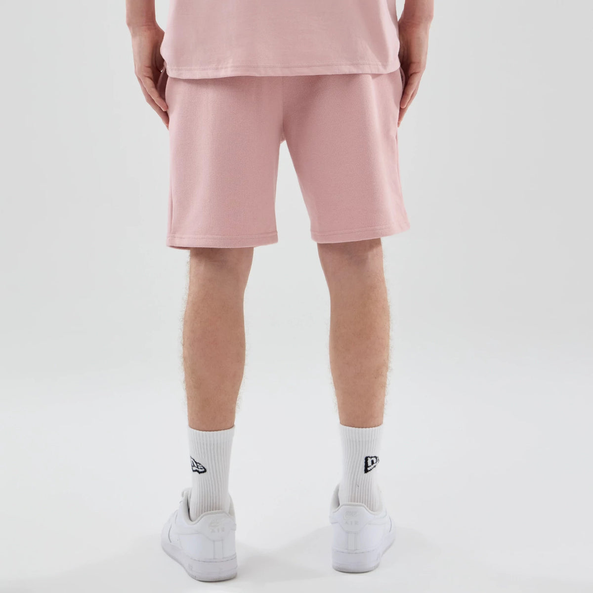 New Era LA Dodgers MLB Midi League Essential Pastel Pink Oversized Shorts, back view on-model showing loose-fitting shorts that fall above the knee, paired with white socks displaying a small embroidered New Era logo and white trainers.