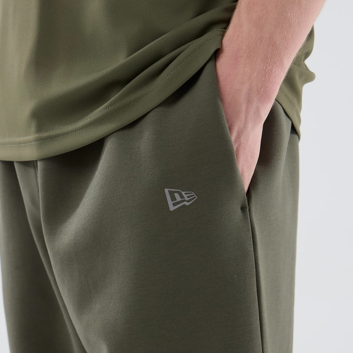 New Era New York Yankees MLB Core Plus Green Joggers, close-up on a model showing the left pocket with a hand inserted, olive green fabric with the white New Era flag logo embroidered near the pocket, and a slightly tapered leg design.
