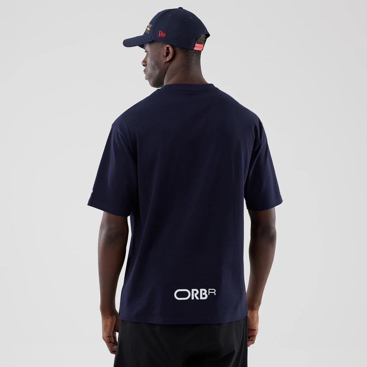 New Era Red Bull Racing Graphic Dark Blue Oversized T-Shirt, back view on a model with a dark blue cap, highlighting a white printed ORBR logo near the hem, loose short sleeves, and a classic crew neck collar for a relaxed fit.