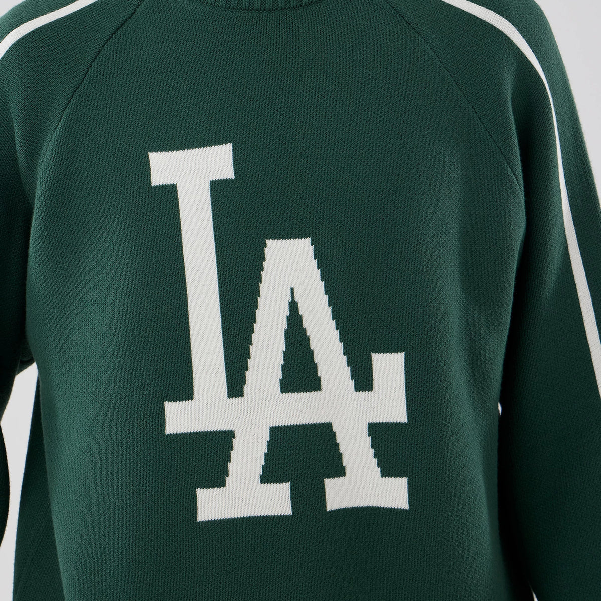 New Era LA Dodgers MLB Knit Dark Green Knitted Sweater, front view showing the large white LA logo in raised knit on the chest, with contrasting white stripes running along the raglan sleeves and a ribbed neckline.