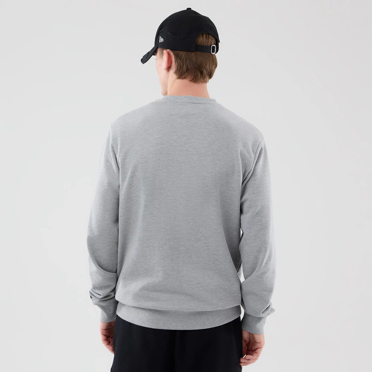 New Era New York Yankees MLB Graphic Grey Oversized Crew Neck Sweater, back view on a model wearing a black cap, showing the plain light grey fabric, relaxed fit with long sleeves, and a ribbed hem and cuffs.