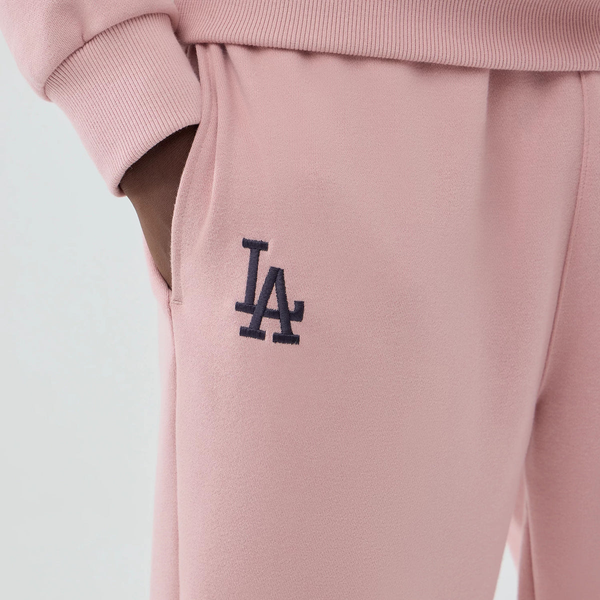 New Era LA Dodgers MLB Midi League Essential Pastel Pink Joggers, close-up view showing the navy LA logo embroidered on the right hip, elastic waistband for comfort, and ribbed cuff details matching the pastel pink colour.