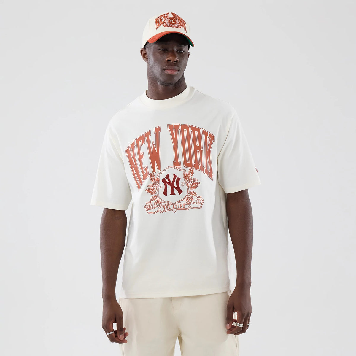 New Era New York Yankees MLB Arch Graphic Open White Oversized T-Shirt, front view on-model displaying red New York lettering and an embroidered Yankees logo on the chest, styled with a matching cap with the same graphic elements.