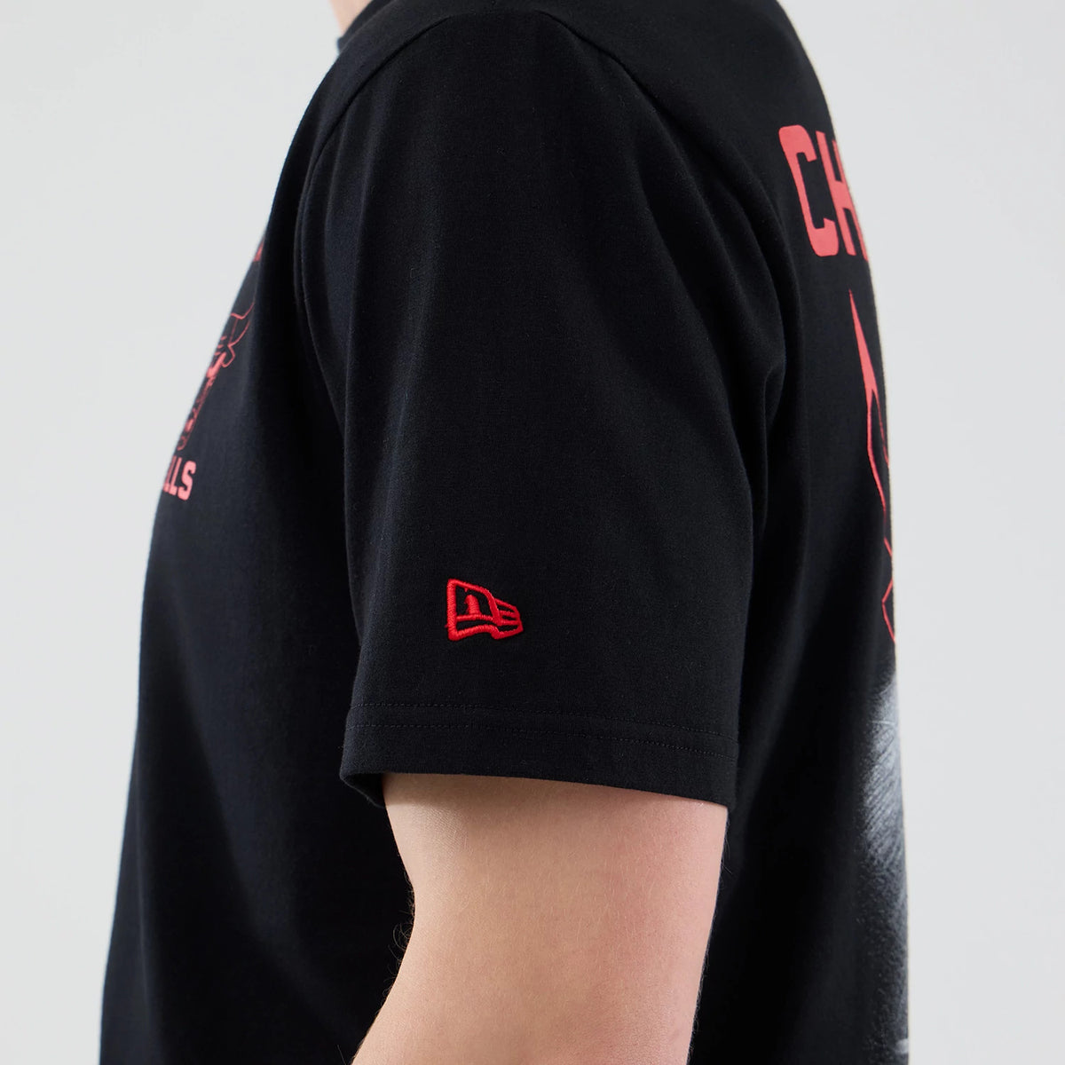 New Era Chicago Bulls NBA Court Graphic Black T-Shirt, side view showing the red Chicago Bulls graphic and CHICAGO text on the back, embroidered red New Era logo on the left sleeve, and the black fabric draping over the shoulder.