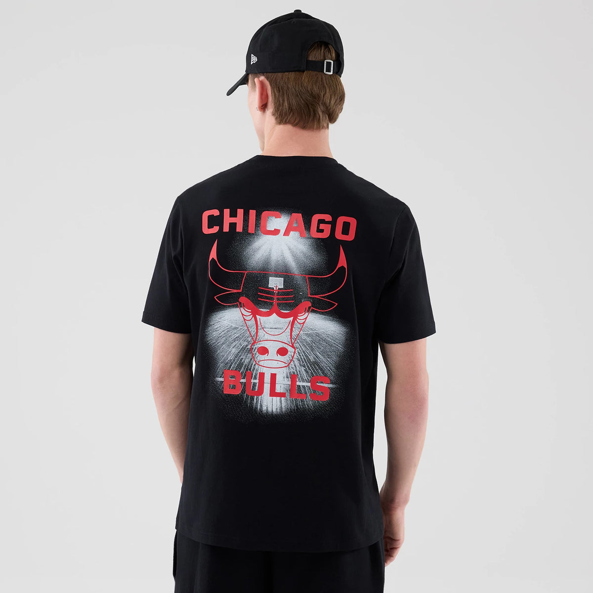 New Era Chicago Bulls NBA Court Graphic Black T-Shirt, back view on a model with a black cap, featuring red Chicago Bulls lettering above a large red outlined bull graphic with an artistic white spray effect highlighting the logo.