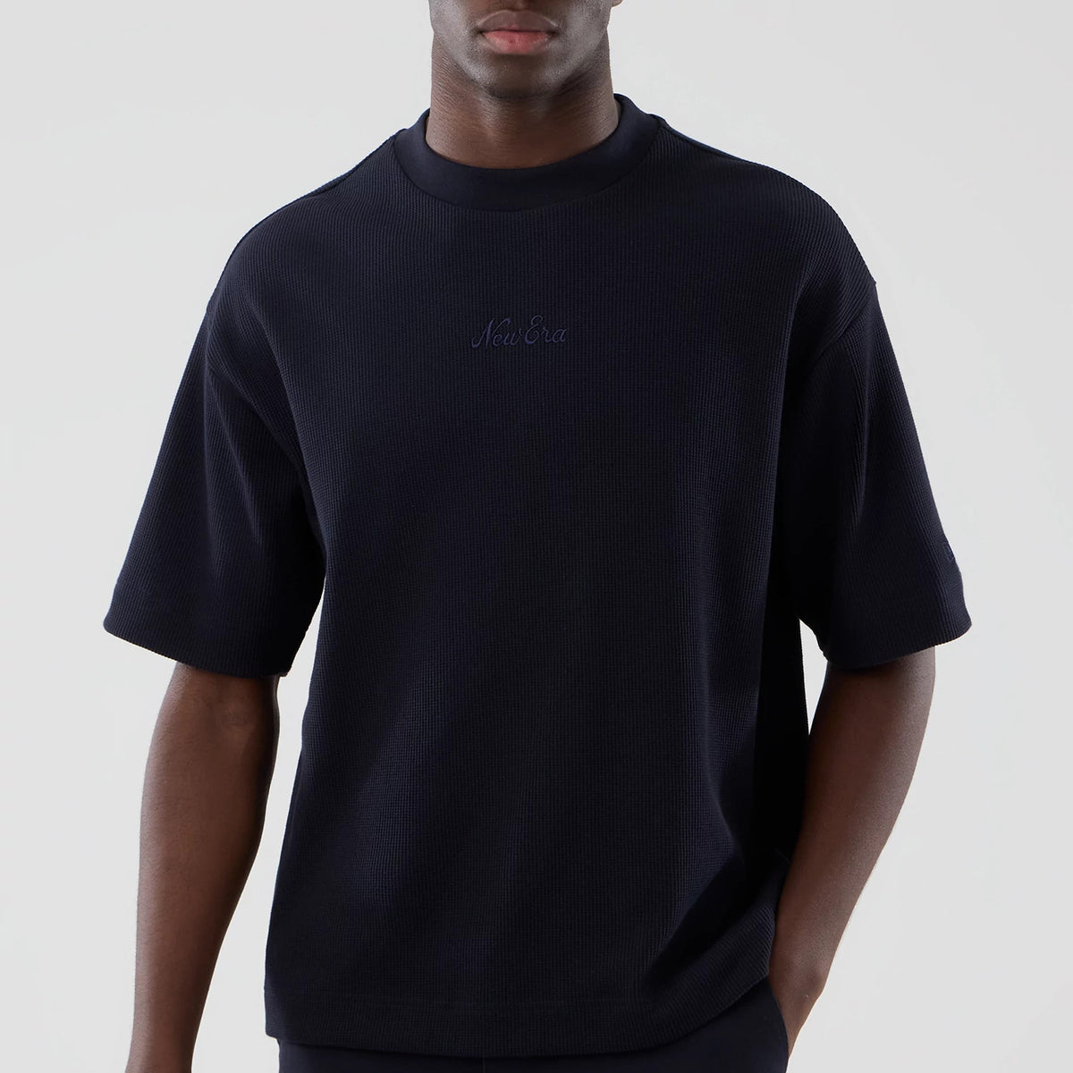 New Era Waffle Navy Boxy T-Shirt, front view showcases its dark navy hue with short sleeves, a raised embroidered New Era logo centred on the upper chest, worn by a model with a relaxed fit and ribbed crew neckline.