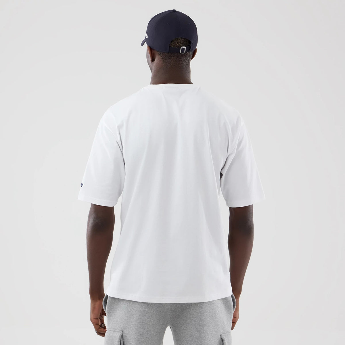 New Era New York Yankees MLB Graphic White Oversized T-Shirt, back view on a model wearing a navy cap, showing a plain white back with short sleeves and a small embroidered New Era logo on the left sleeve.