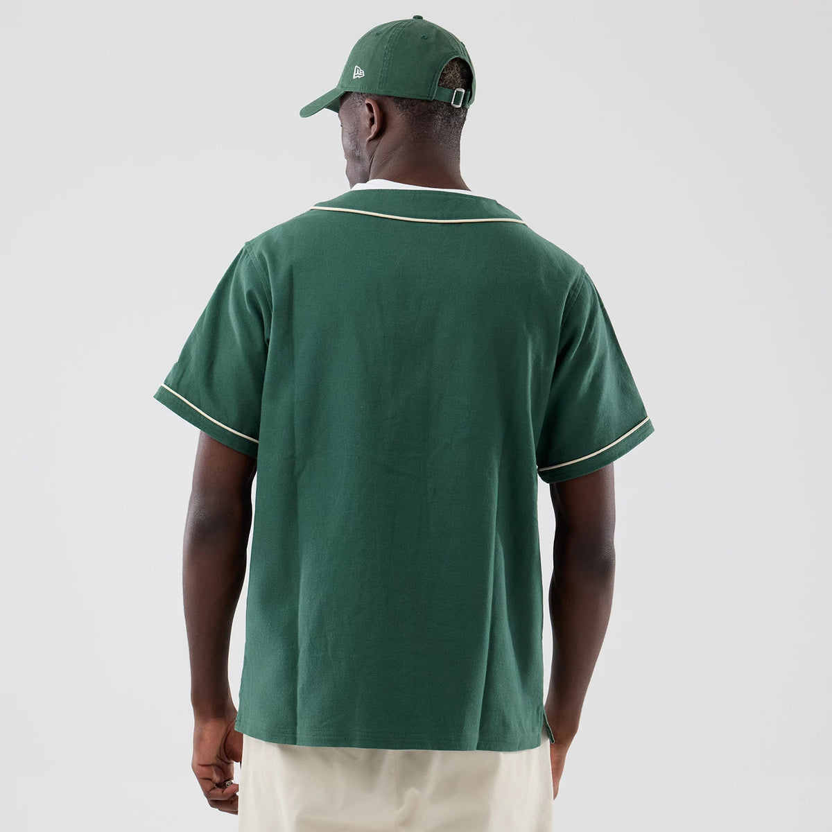 New Era Dark Green Baseball Jersey, back view on a model with a matching cap, featuring a relaxed fit with white piping along the collar and sleeve edges, enhancing the classic baseball style with a plain back design.