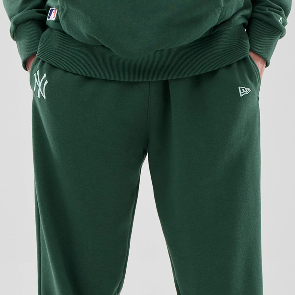 New Era New York Yankees MLB Midi League Essential Dark Green Joggers, front view on a model showing the white embroidered NY logo on the left thigh, the New Era flag logo on the right hip, and ribbed waistband with hands in pockets.