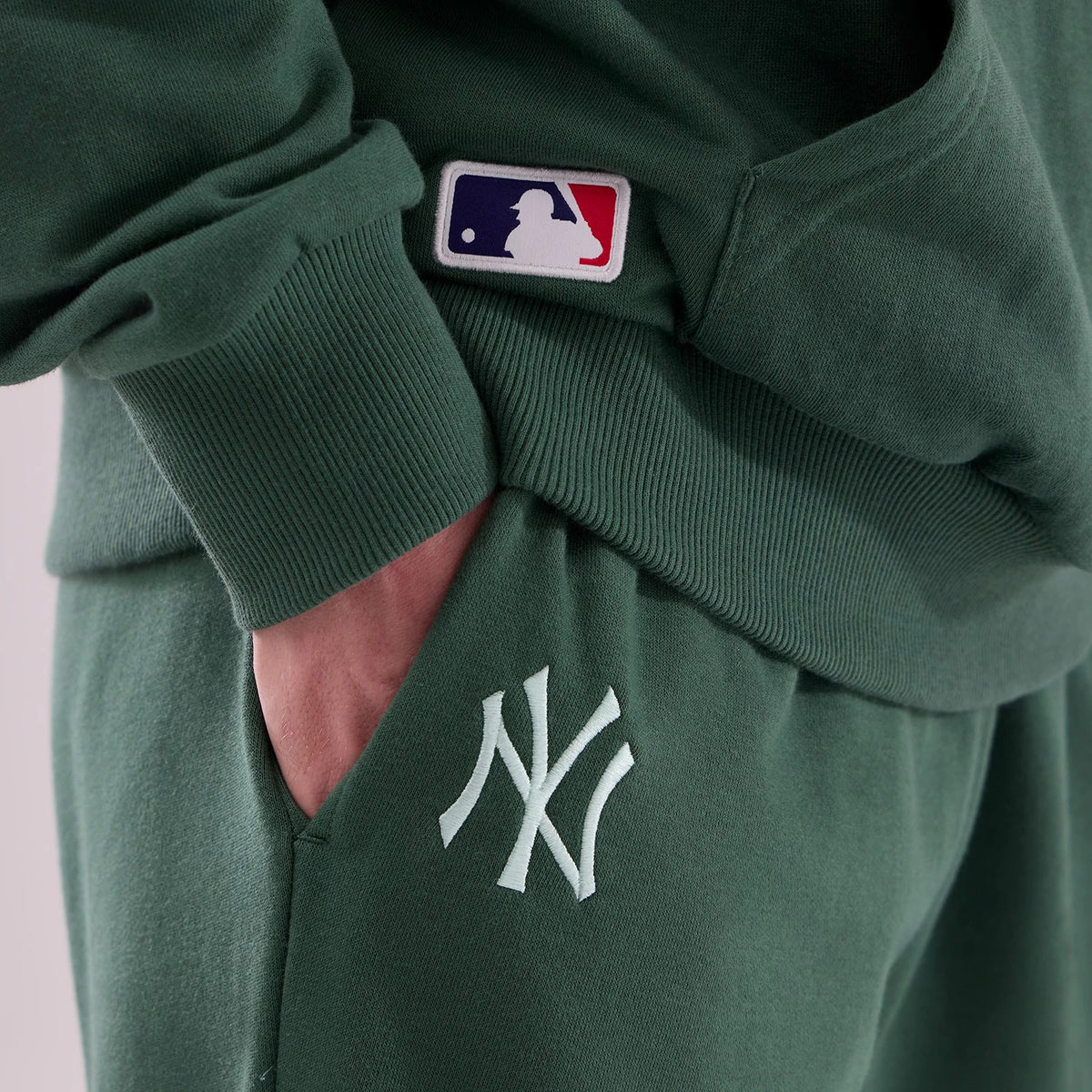 New Era New York Yankees MLB Midi League Essential Dark Green Joggers, close-up view showing the white NY logo embroidery on the thigh, with ribbed cuffs at the waist and a small MLB logo patch above the pocket.