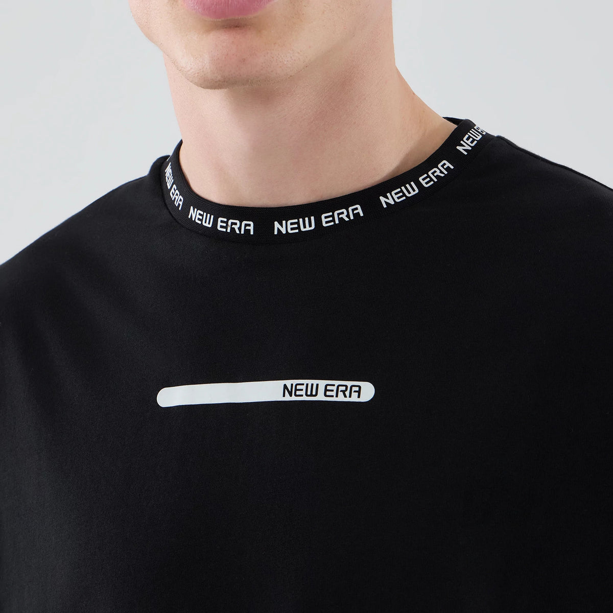 New Era Tech Black T-Shirt, front view showing a model wearing the black t-shirt with a white printed New Era logo on the chest, repeated white New Era lettering around the neck, and a close fit at the collar.