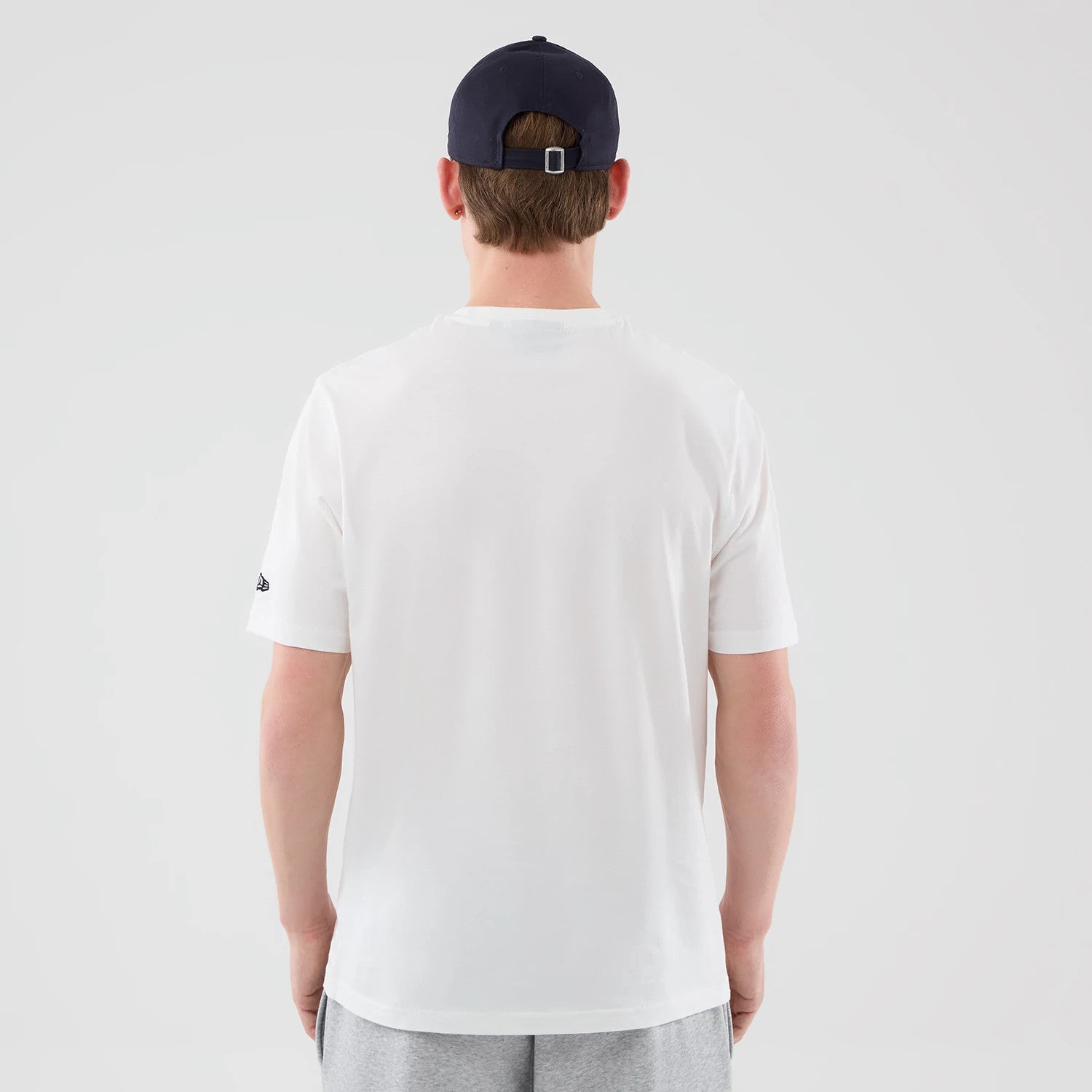 New Era New York Yankees MLB Graphic White T-Shirt, back view on a model paired with a dark cap and grey shorts, displaying a plain white back with an embroidered New Era logo on the left sleeve.