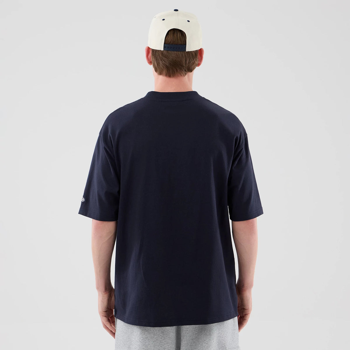 New Era New York Yankees MLB Arch Graphic Navy Oversized T-Shirt, back view on a model wearing a light cap and grey shorts, showing the plain navy back with a loose fit and a small embroidered New Era logo on the left sleeve.