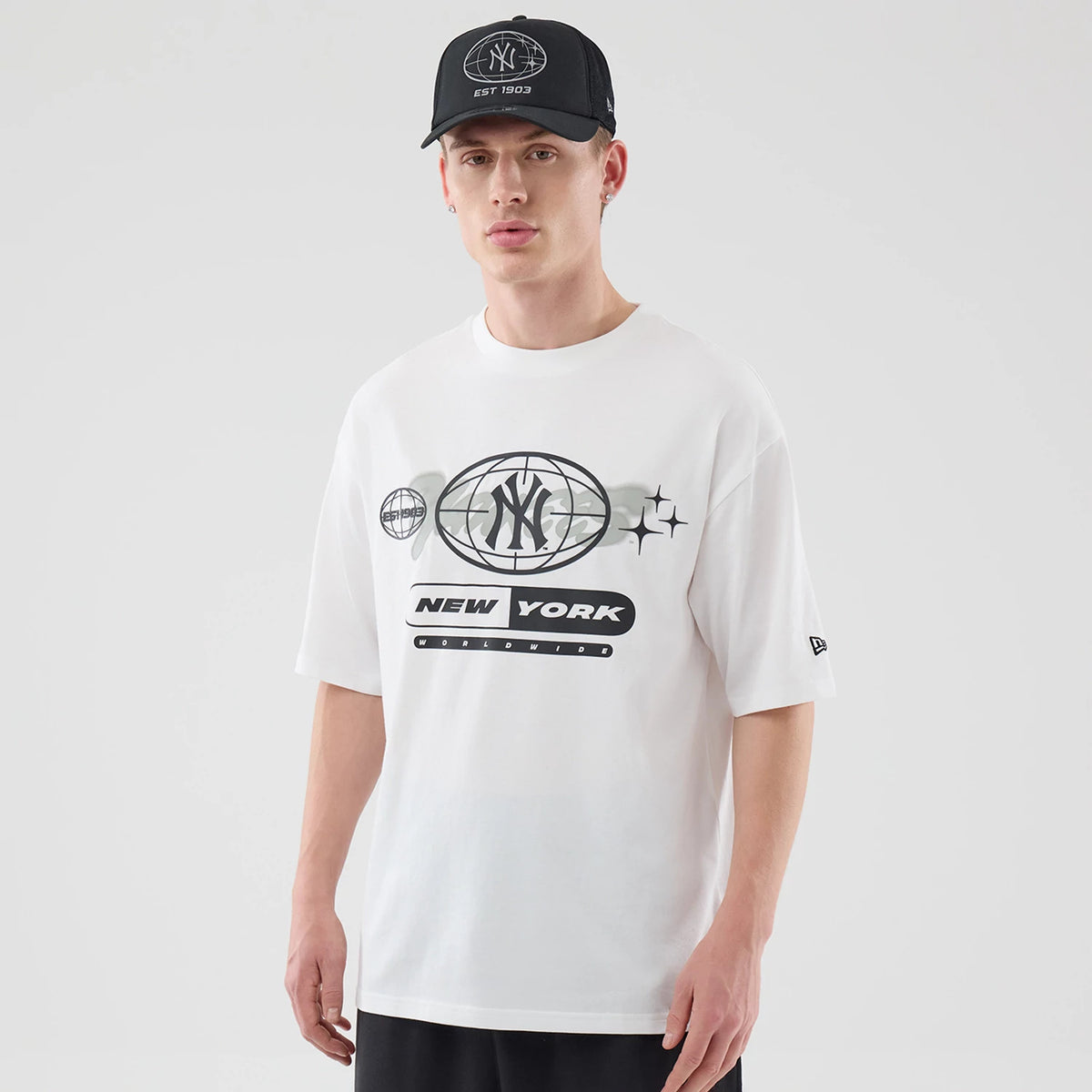 New Era New York Yankees MLB Logo Graphic White Oversized T-Shirt, front view on-model showing a large printed Yankees logo and New York text across the chest in black, with an embroidered New Era logo on the left sleeve.