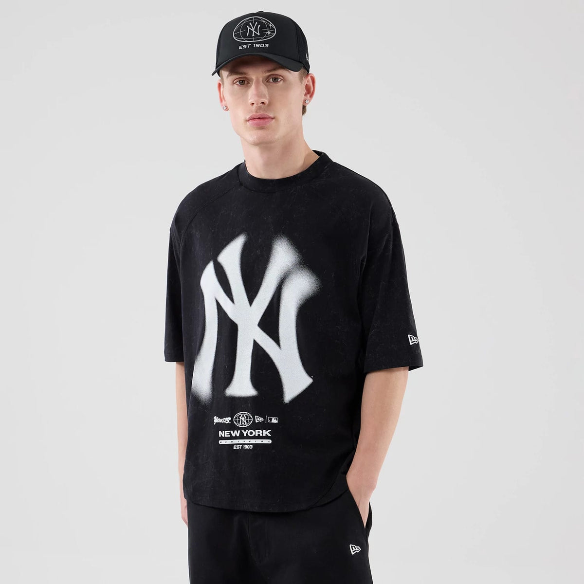 New Era New York Yankees MLB Graphic Boxy Black T-Shirt, front view on a model with a black cap, featuring a large white NY logo on the chest, additional branding above the hem, and an embroidered New Era logo on the left sleeve.