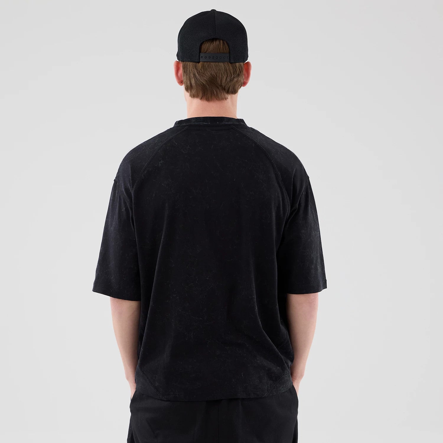 New Era New York Yankees MLB Graphic Boxy Black T-Shirt, back view on-model showing the loose fit with a faded pattern, short sleeves falling below the elbow, and a straight hemline, paired with a black cap that features an adjustable strap.