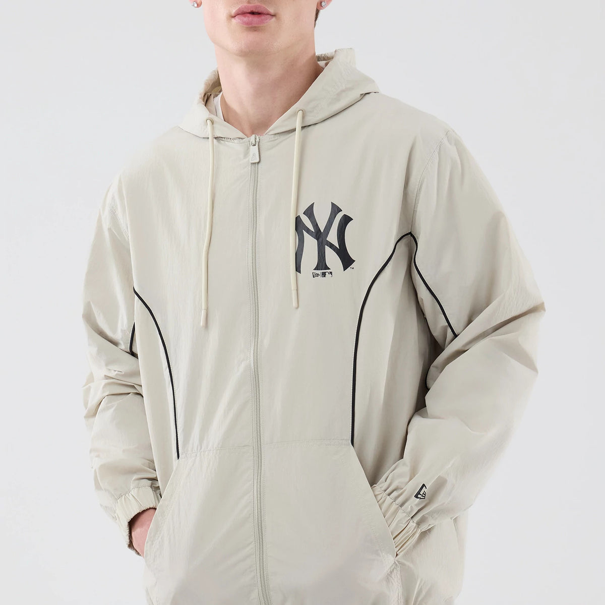 New Era New York Yankees MLB Piping Cream Jacket, three-quarter view on-model showing the front zip closure, black embroidered Yankees logo on the left chest, black piping details running down the sleeves.