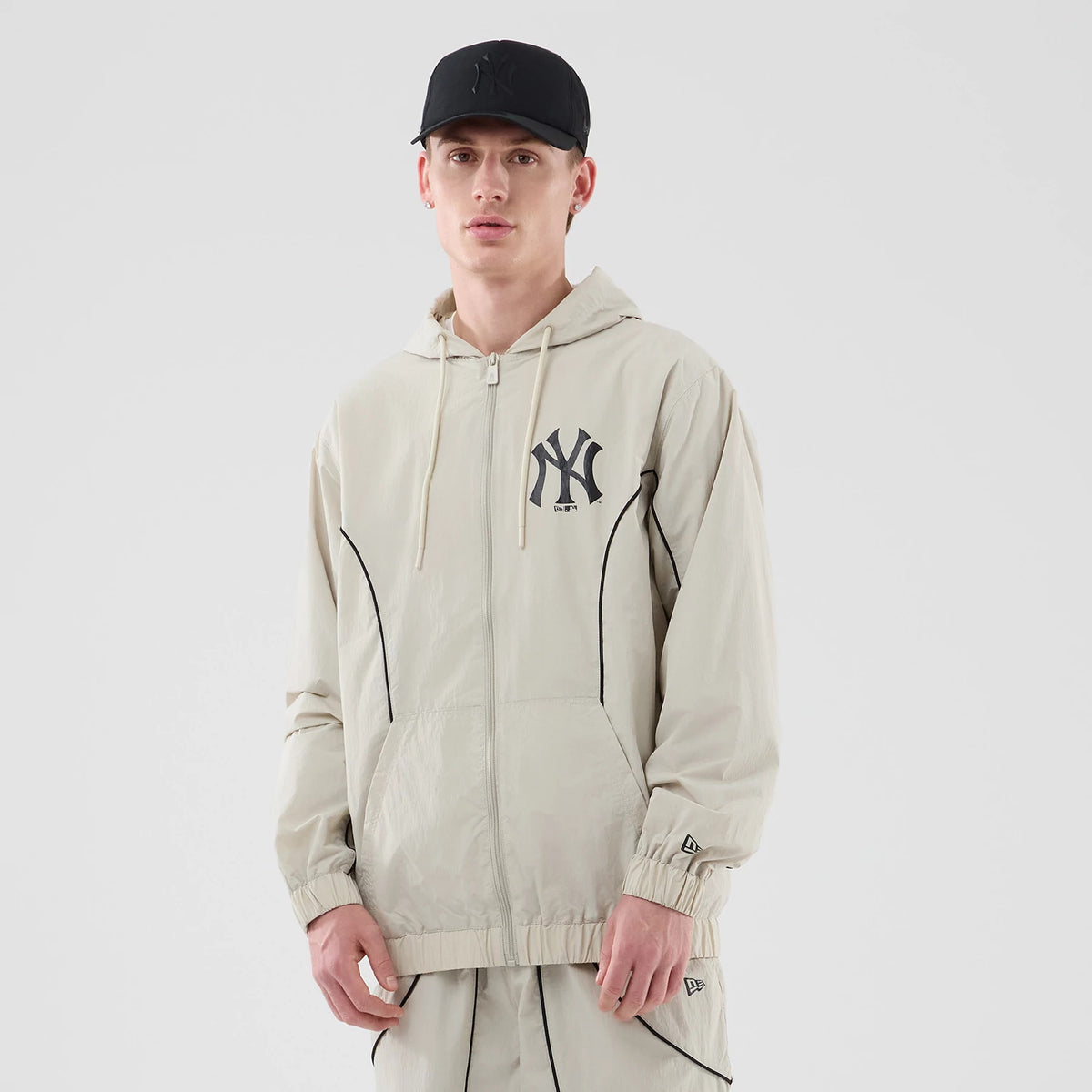 New Era New York Yankees MLB Piping Cream Jacket, front view on-model showing the Yankees logo embroidered on the left chest, black piping down the front, a full zip closure and the New Era flag embroidered on the left sleeve cuff.